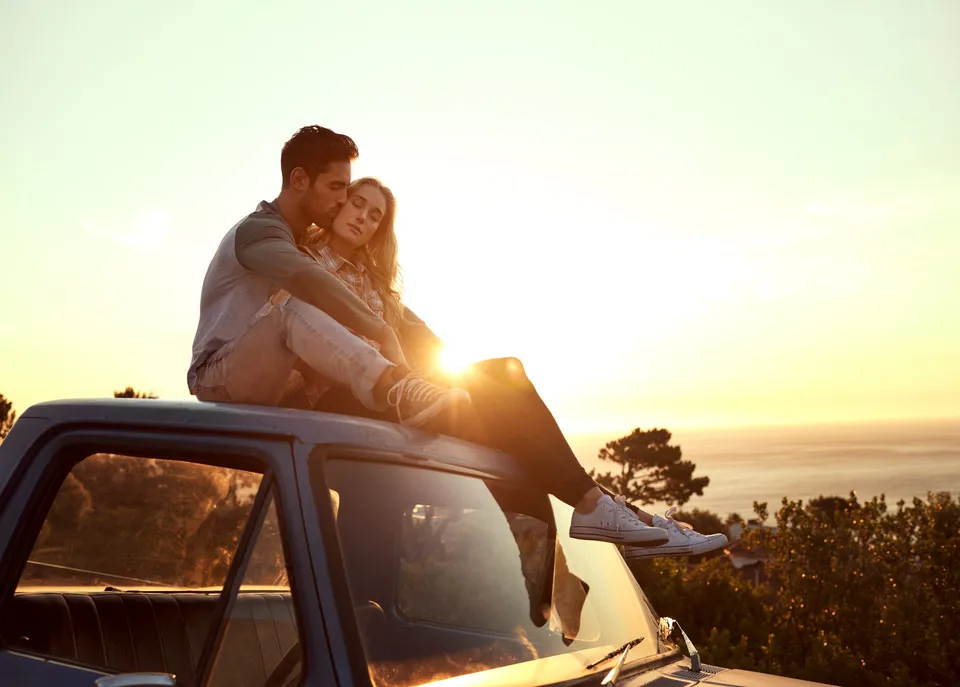 Couple embracing on a truck at sunset overlooking the coast