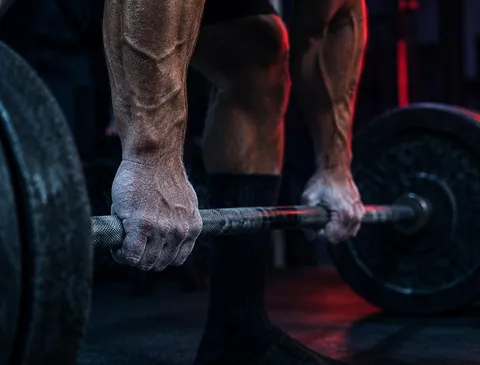 Chalked hands gripping a loaded barbell in a dark tactical gym