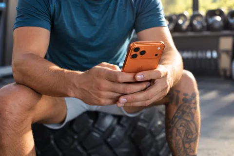Man in athletic wear sitting on a tire at the gym, starting a health intake on his phone